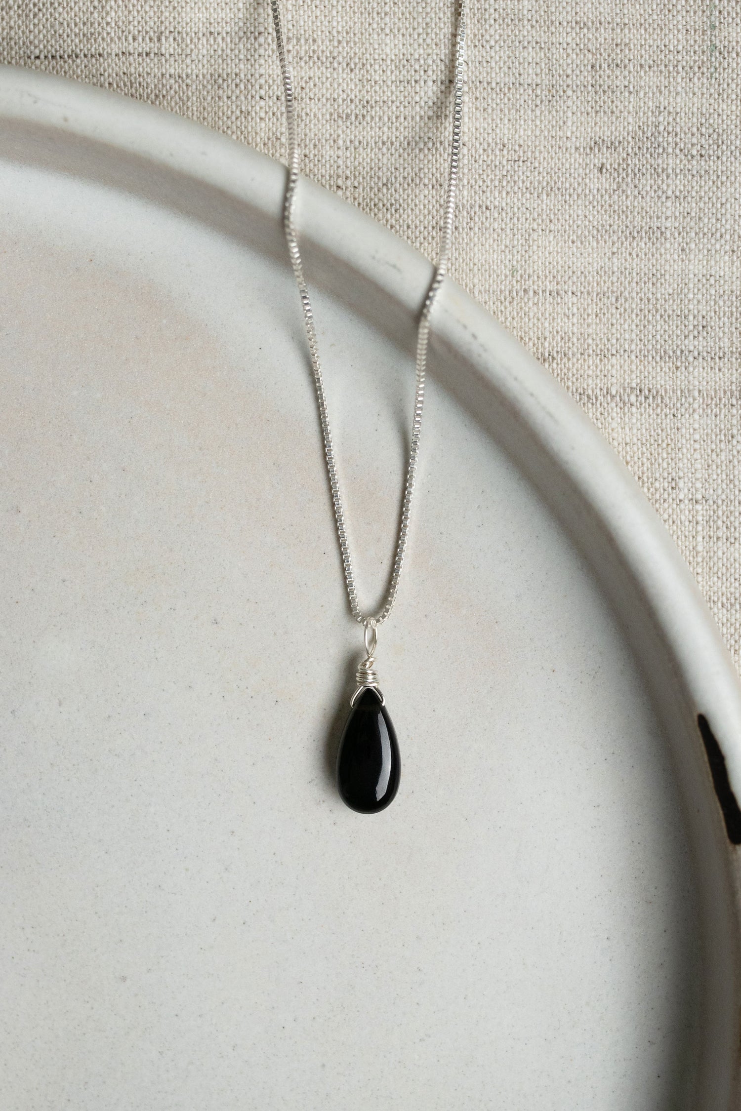 A handcrafted minimalist black obsidian teardrop necklace on a delicate sterling silver chain, showcasing the stone’s smooth, volcanic glass finish.
