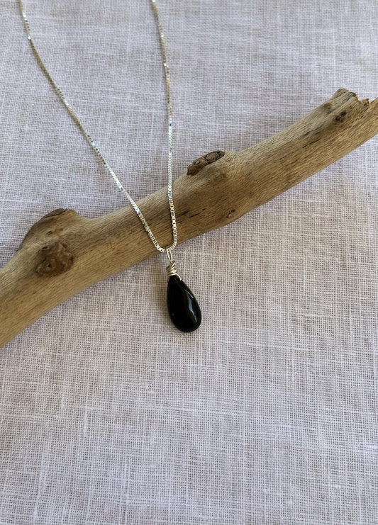 A handcrafted minimalist black obsidian teardrop necklace on a delicate sterling silver chain, showcasing the stone’s smooth, volcanic glass finish.