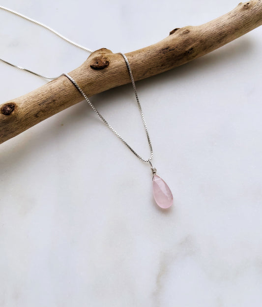 A handcrafted Rose Quartz teardrop necklace with a hand-cut gemstone on a gold-filled chain, showing the delicate pink color.