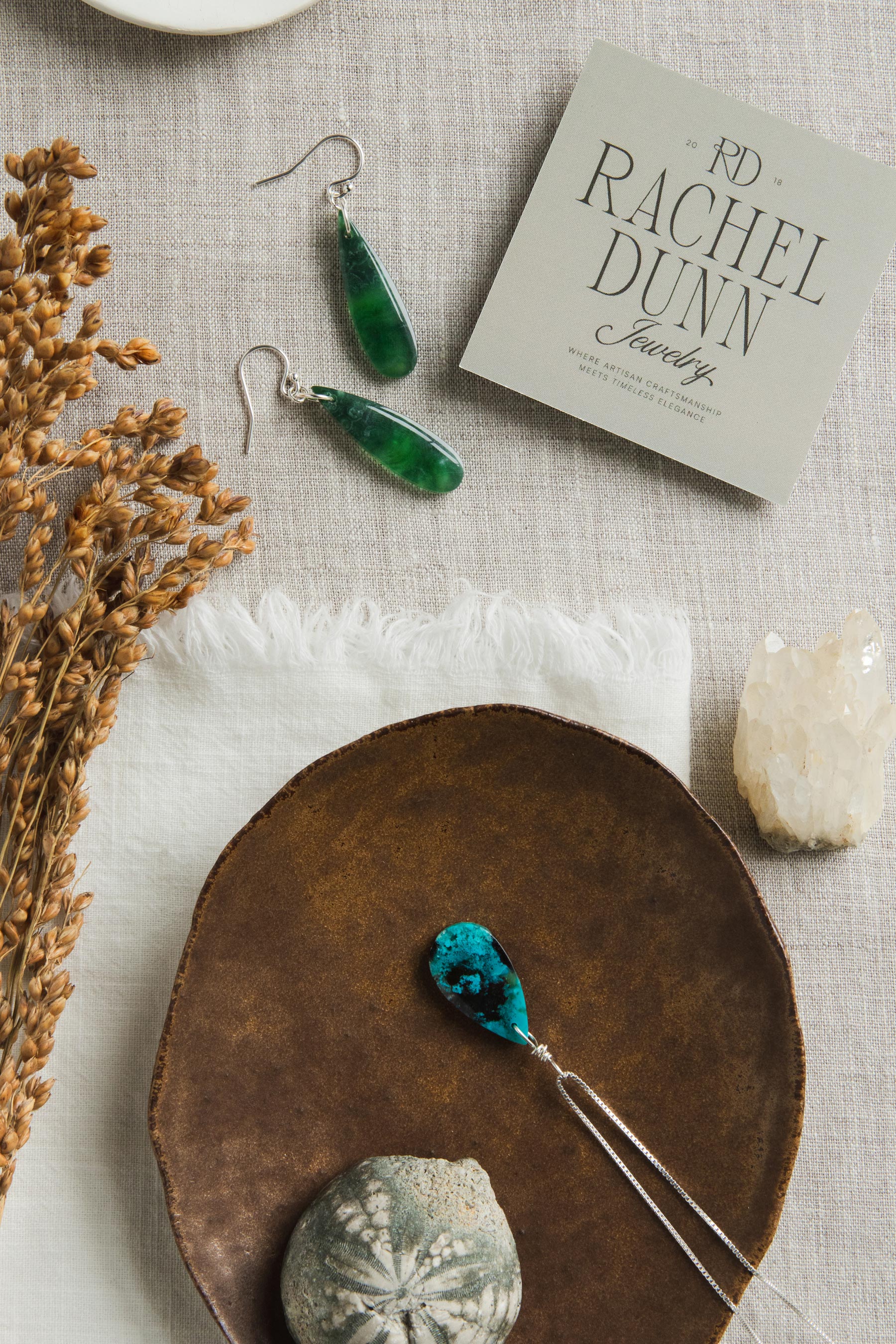 Green earrings on a textured surface with a Rachel Dunn jewelry box and decorative items.