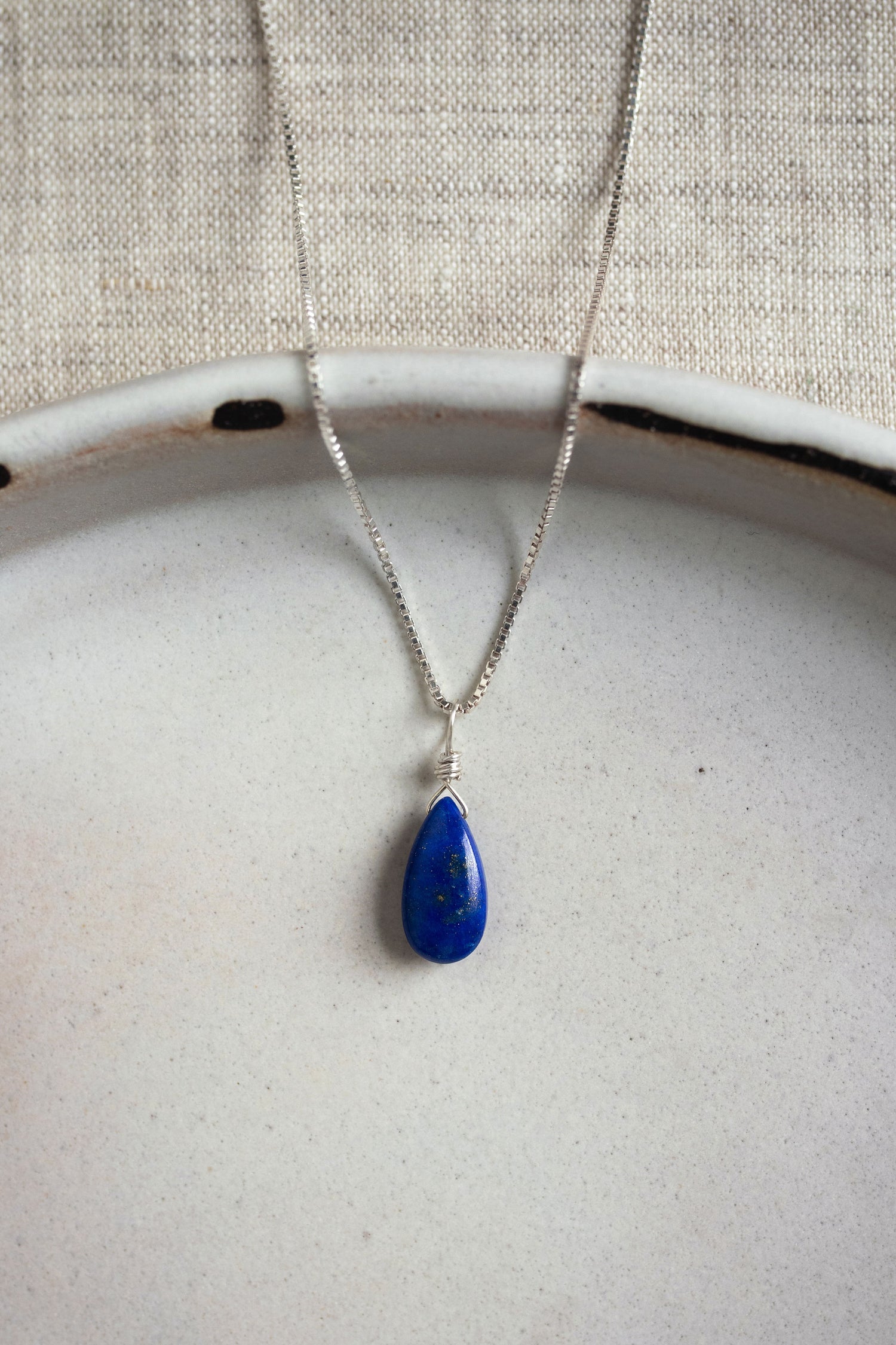 A handcrafted teardrop Lapis Lazuli necklace with a deep blue gemstone, wire-wrapped and hanging from a delicate silver chain.