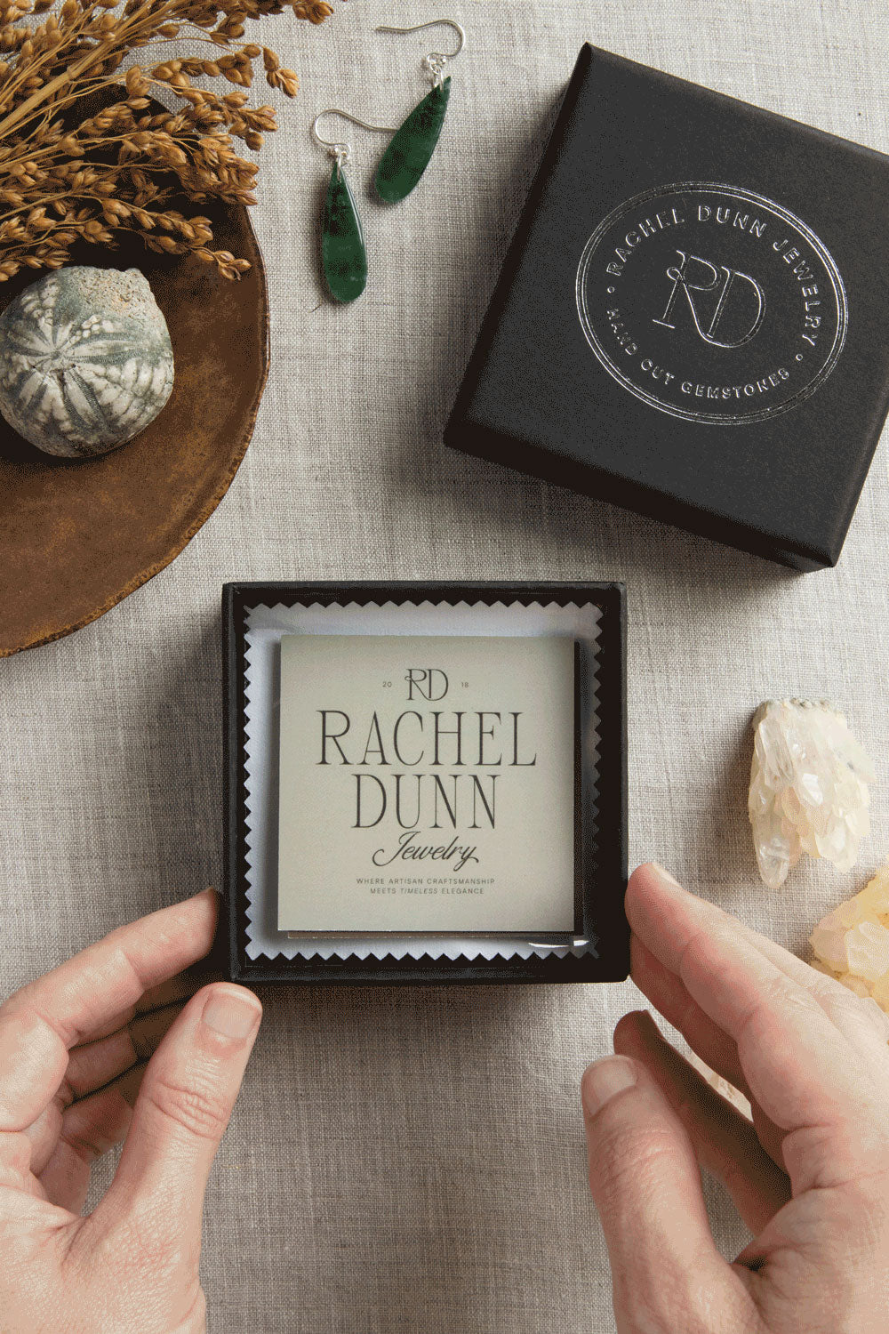 Jewelry box with 'Rachel Dunn Jewelry' branding, earrings, and decorative items on a textured surface.