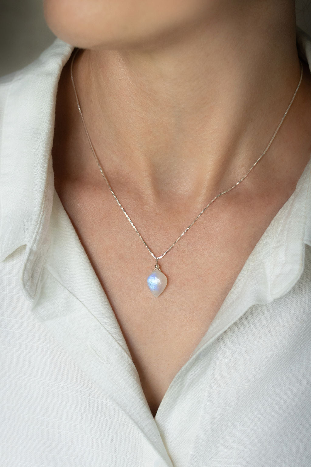 A person wearing a handcrafted leaf-shaped Rainbow Moonstone necklace with a wire-wrapped crystal pendant on a .925 sterling silver box chain.