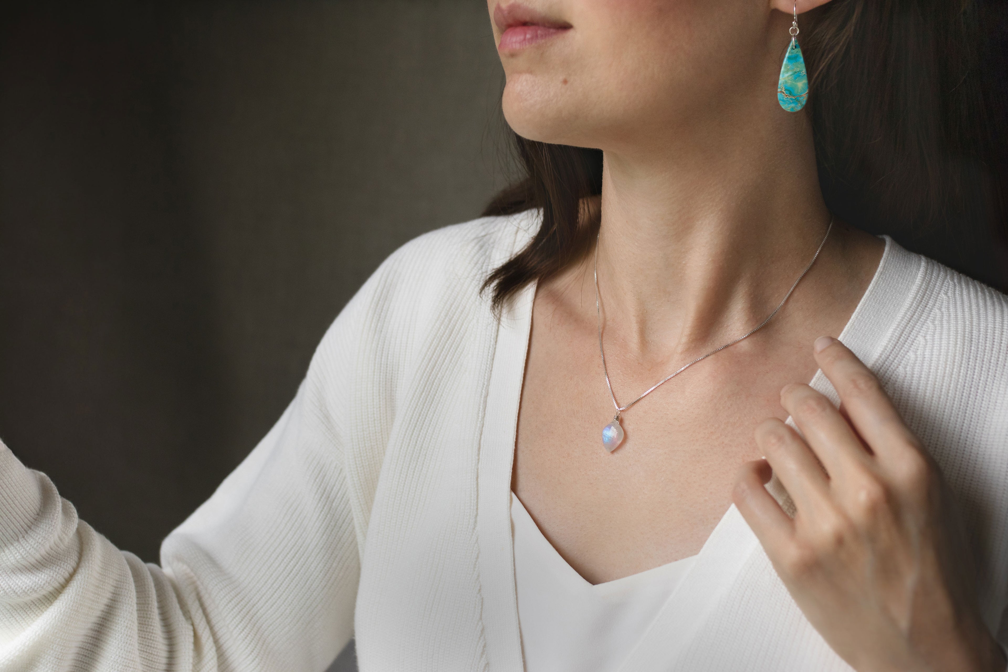 Woman wearing a necklace with a pendant and turquoise earrings against a dark background