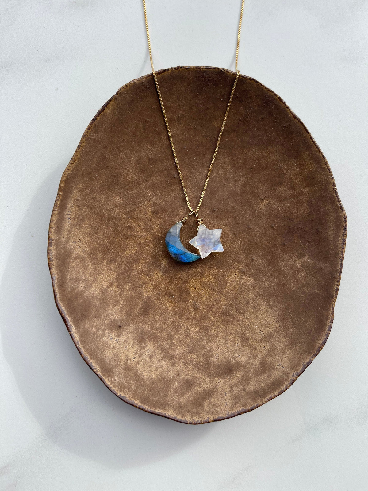 Labradorite Moon + Moonstone Star pendants on a gold chain laying on a brown bowl