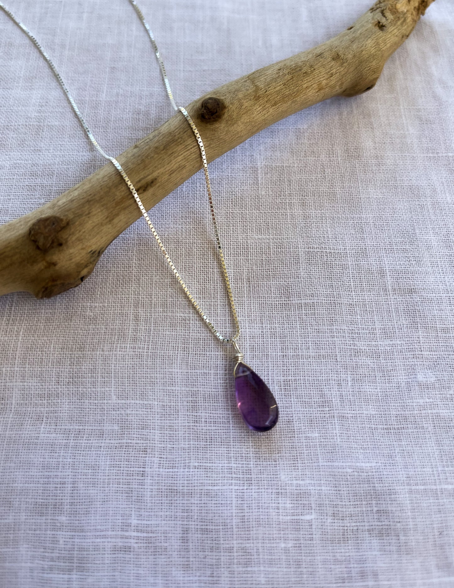 A handcrafted amethyst teardrop necklace featuring a natural violet-colored gemstone on a delicate sterling silver chain