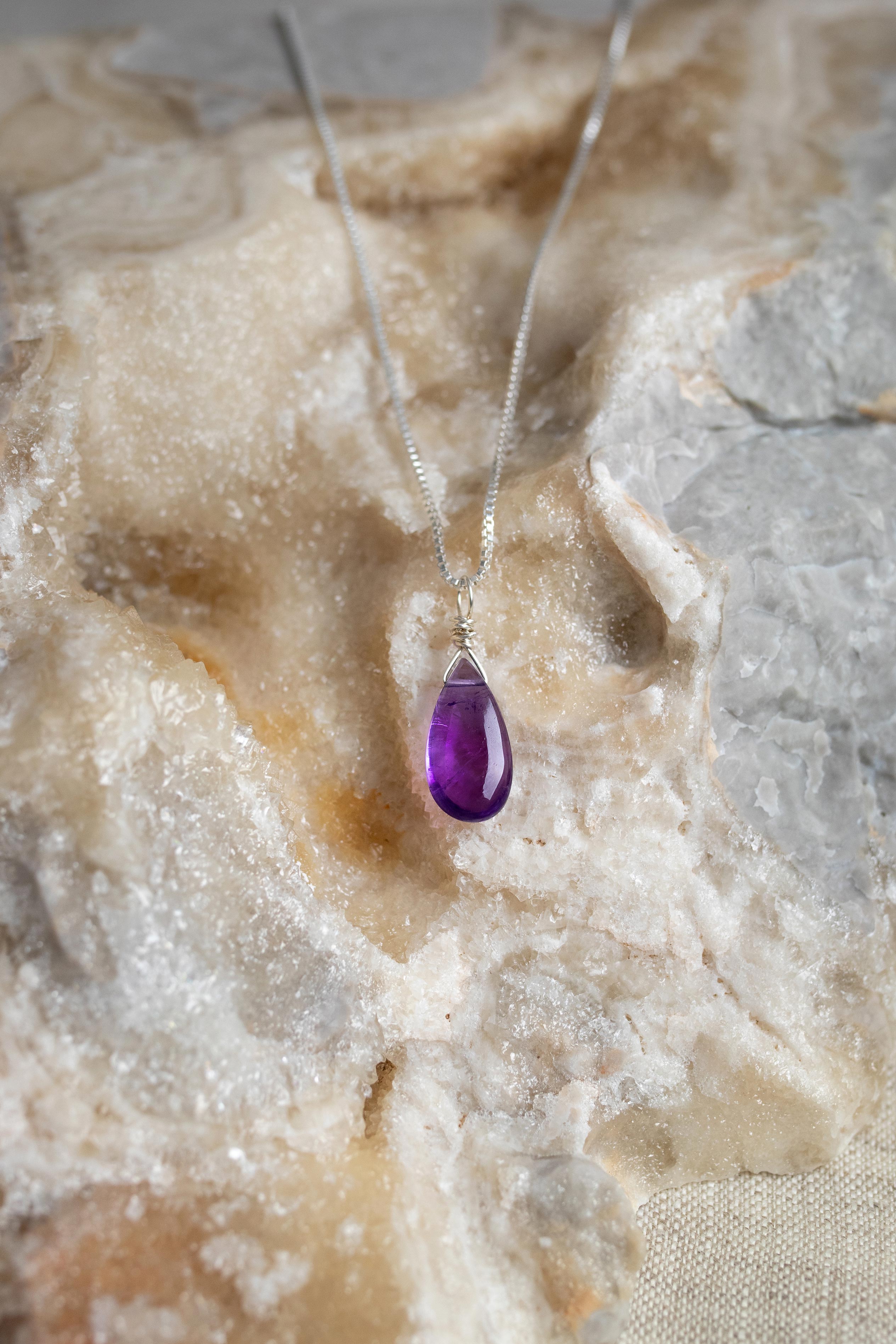 Amethyst teardrop pendant on a silver chain against a textured stone background