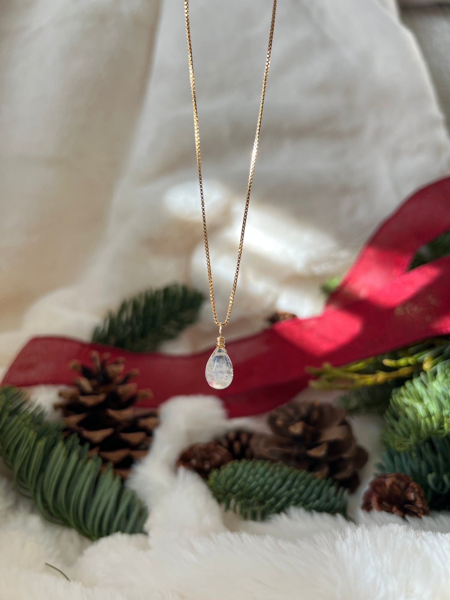 Gold necklace with a pendant on a Christmas-themed background with greenery and pinecones.