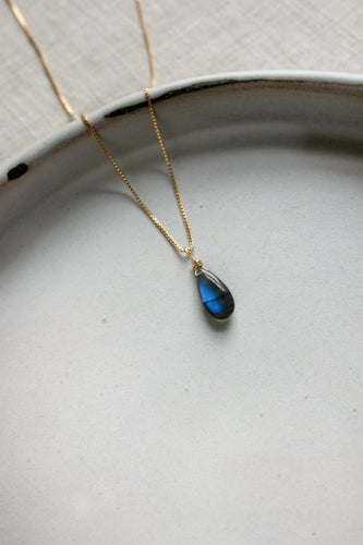 Gold chain necklace with a labradorite teardrop pendant on a ceramic white plate