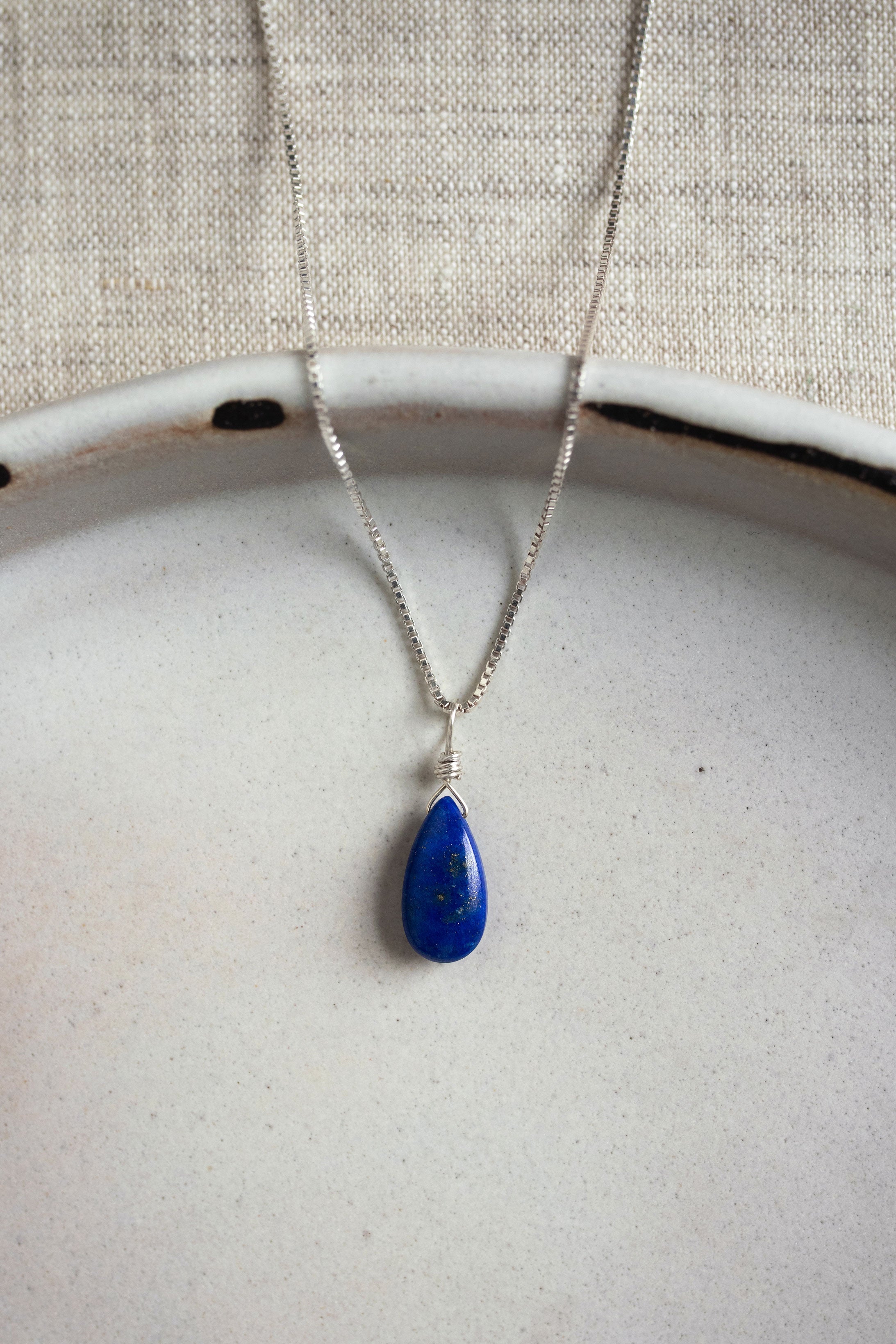 A handcrafted teardrop Lapis Lazuli necklace with a deep blue gemstone, wire-wrapped and hanging from a delicate silver chain.