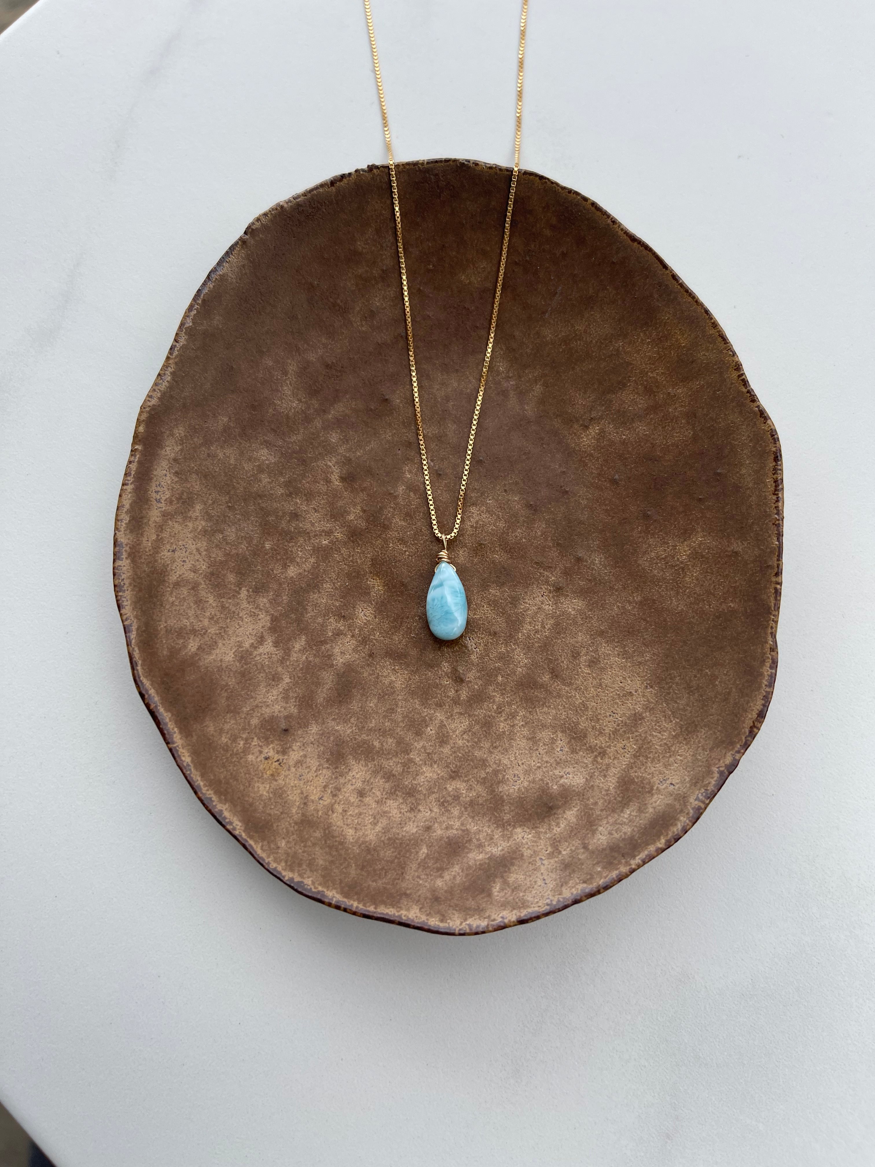 Necklace with a blue Larimar pendant necklace on a brown cushion