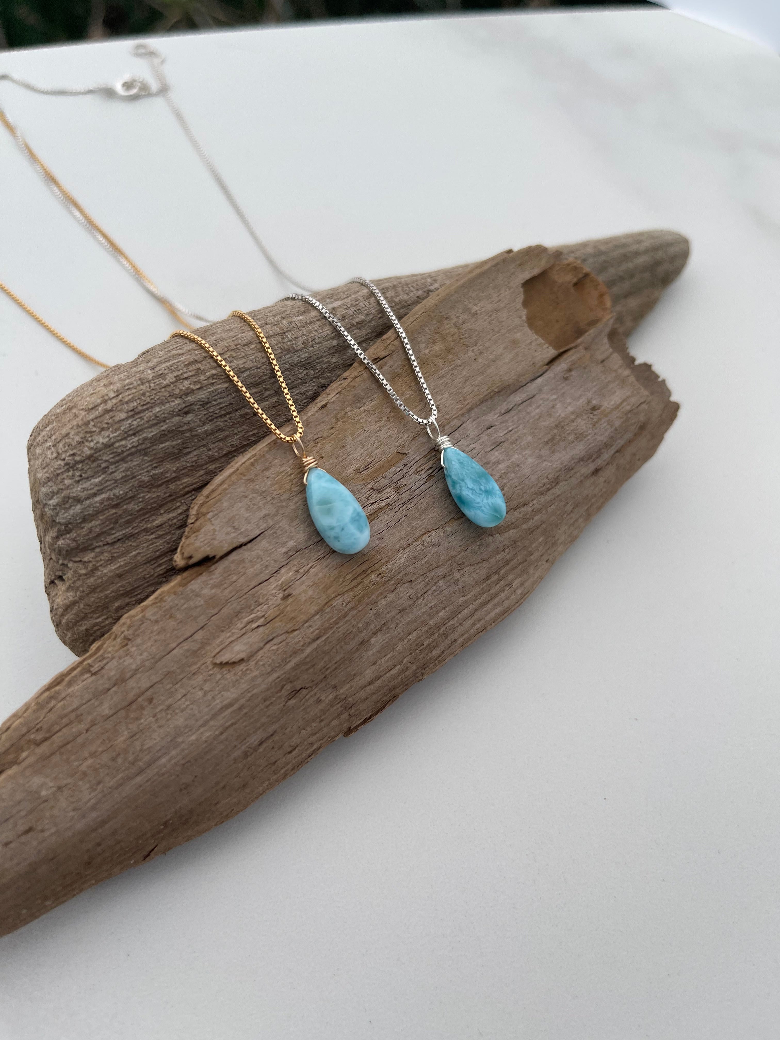 Two necklaces with blue Larimar stones on a piece of driftwood against a white background
