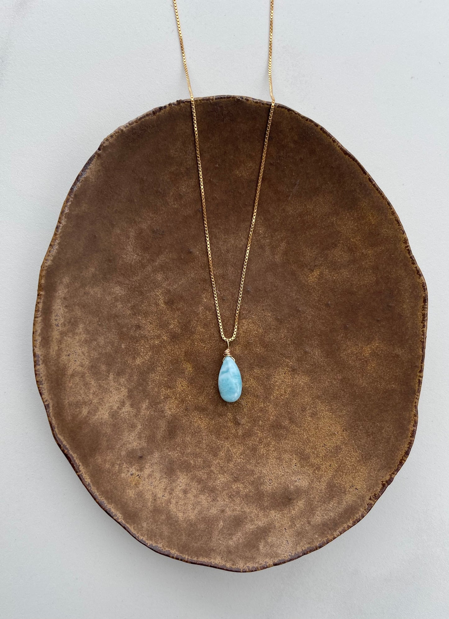 Necklace with a blue Larimar pendant on a brown bowl against a light gray background
