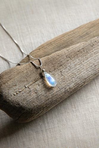 Silver chain necklace with a moonstone pendant on a wooden surface