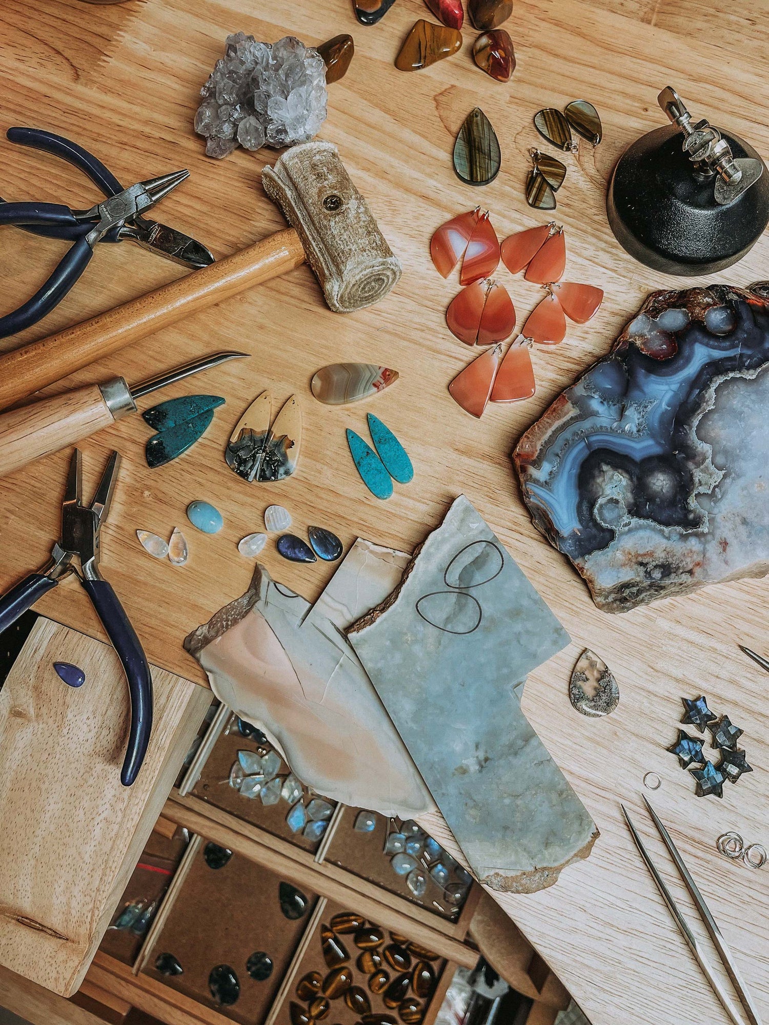 Workbench with gemstones, tools, and jewelry components on a wooden surface