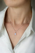 Load image into Gallery viewer, A teardrop-shaped rainbow moonstone necklace with a vibrant iridescent flash, hand wire-wrapped and hanging from a box chain with a spring-ring clasp, on a person wearing a white shirt.
