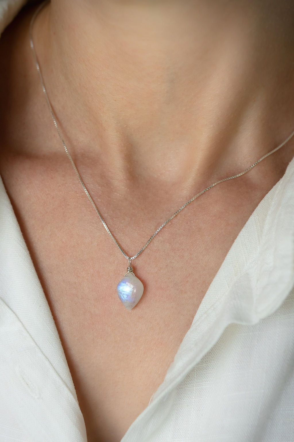 Necklace with a moonstone pendant worn by a person wearing a white shirt