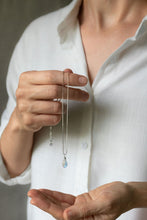 Load image into Gallery viewer, Person holding a teardrop-shaped rainbow moonstone necklace with a vibrant iridescent flash, hand wire-wrapped and hanging from a box chain with a spring-ring clasp.
