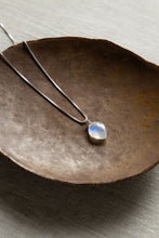 Load image into Gallery viewer, A handcrafted leaf-shaped Rainbow Moonstone necklace with a wire-wrapped crystal pendant on a .925 sterling silver box chain, set on a brown bowl.
