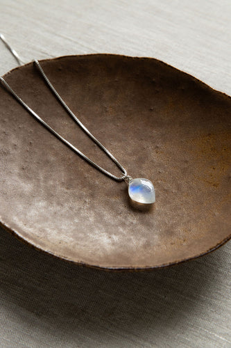Silver chain necklace with a moonstone pendant on a textured surface