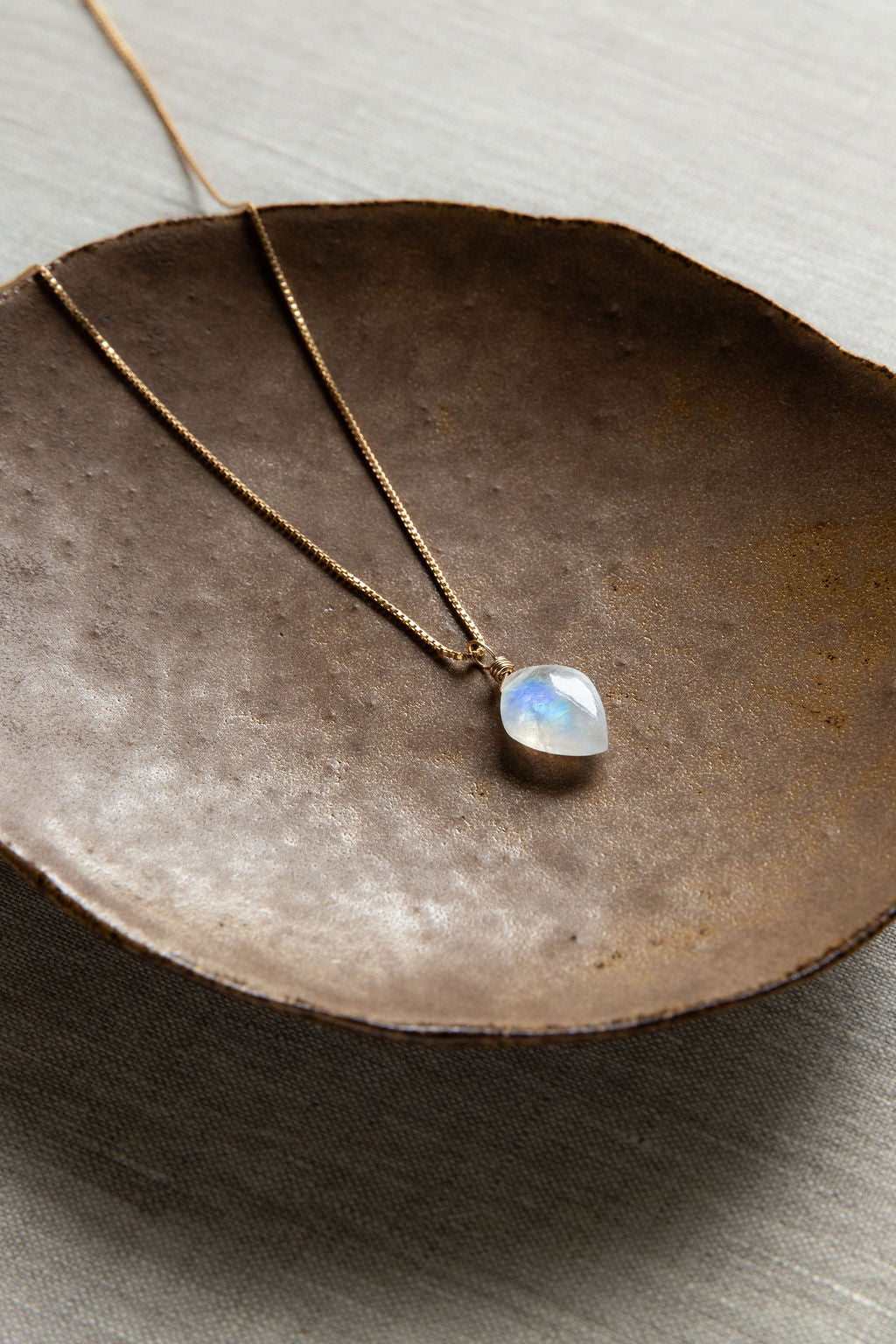 A handcrafted leaf-shaped Rainbow Moonstone necklace with a wire-wrapped crystal pendant on a 14kt gold filled box chain.