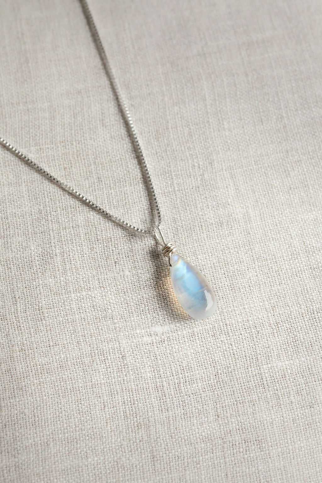 Necklace with a teardrop-shaped moonstone pendant on a light fabric background