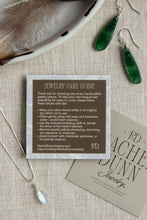 Load image into Gallery viewer, Jewelry care guide card with green earrings and necklace on a textured surface
