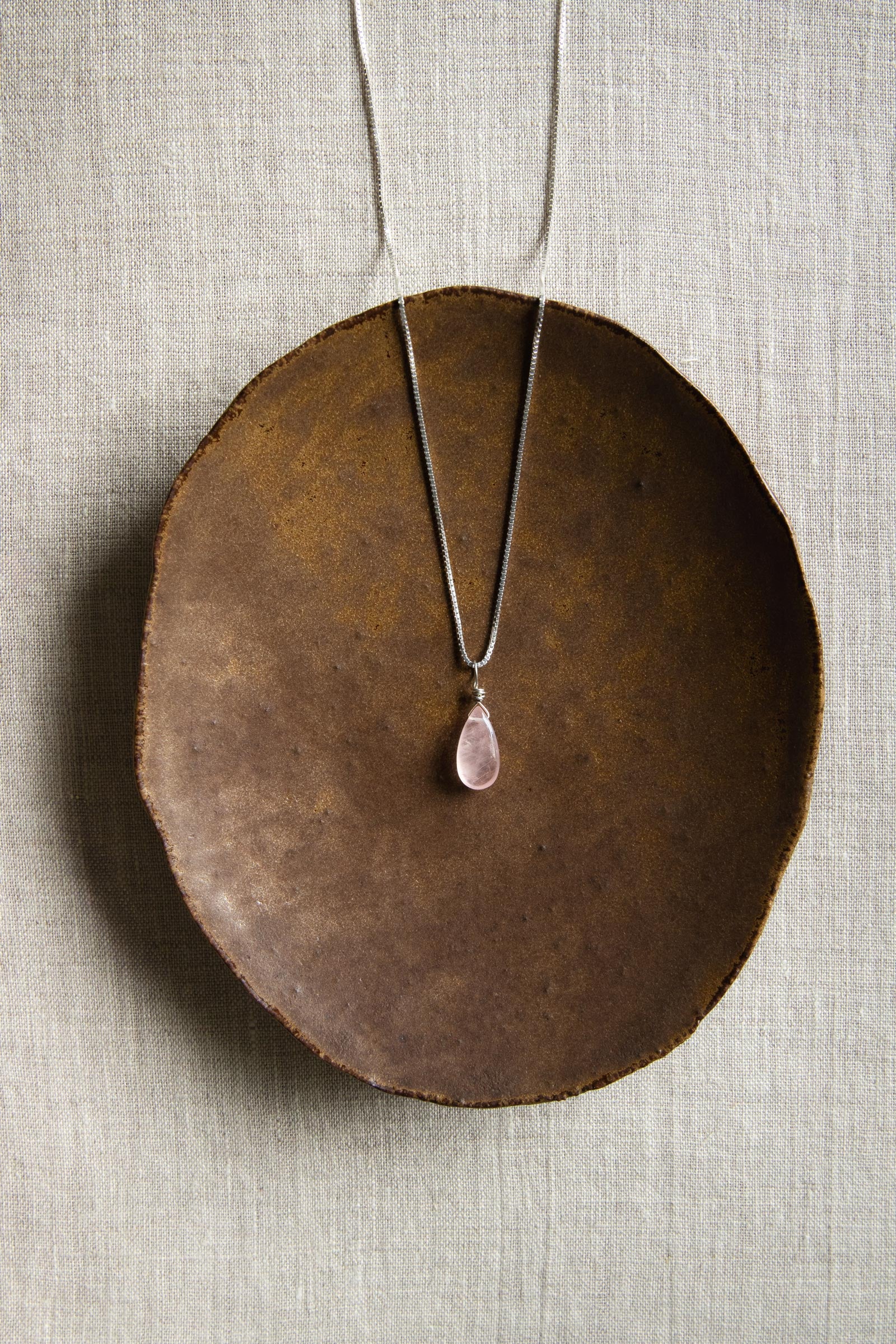 A handcrafted Rose Quartz teardrop necklace with a hand-cut gemstone on a sterling silver chain, showing the delicate pink color.