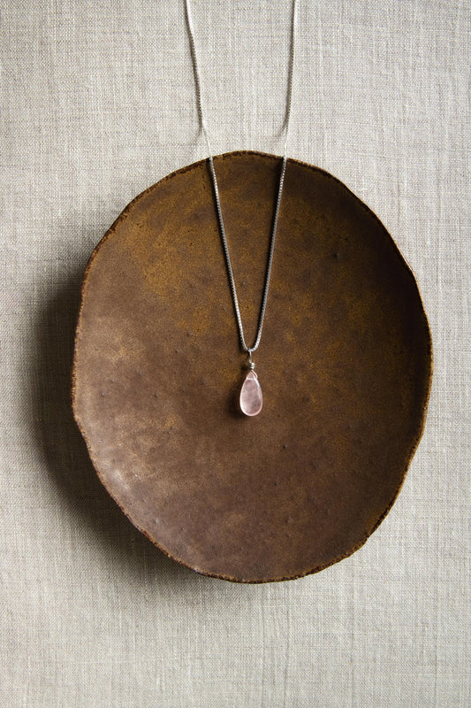 A handcrafted Rose Quartz teardrop necklace with a hand-cut gemstone on a sterling silver chain, showing the delicate pink color.