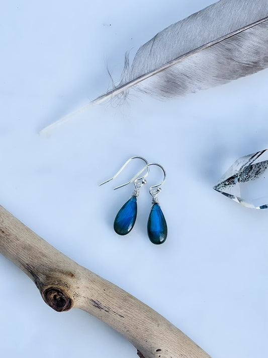 A pair of minimalist handcrafted labradorite teardrop earrings with a natural blue flash, hanging from sterling silver French ear wires.