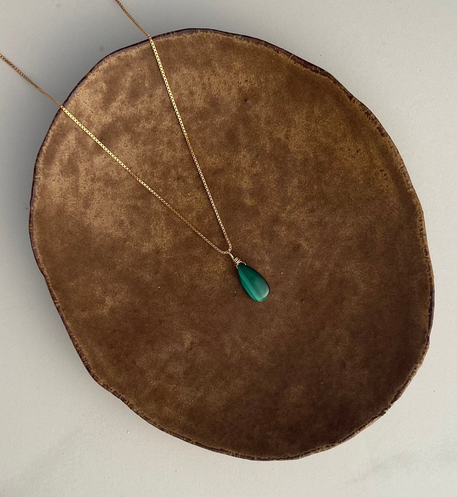 Gold necklace with a green malachite pendant on a brown plate